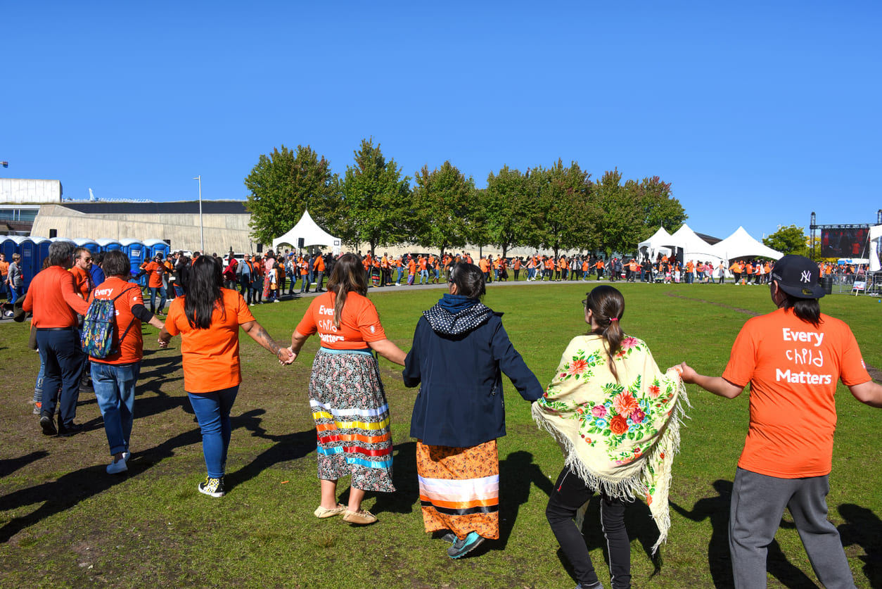 People in orange shirts hold hands in a circle, honoring National Day for Truth and Reconciliation.