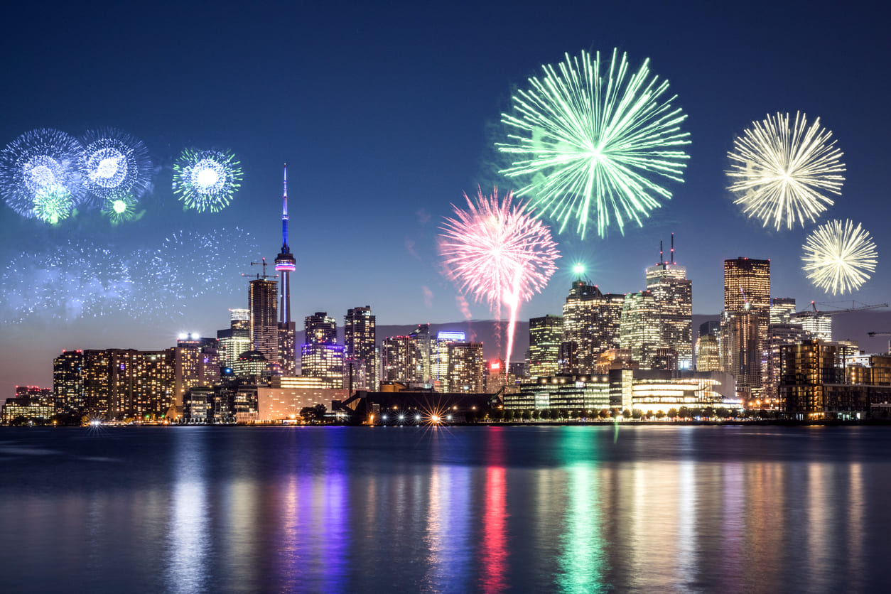 A stunning view of the Toronto skyline illuminated by vibrant New Year's Eve fireworks, reflecting beautifully over the waterfront.