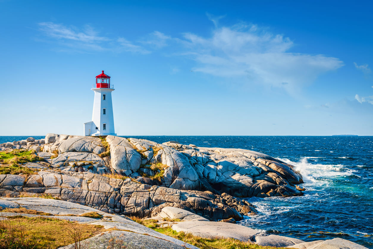 The Peggy's Cove lighthouse stands peacefully under a clear summer sky, overlooking the calm waters.