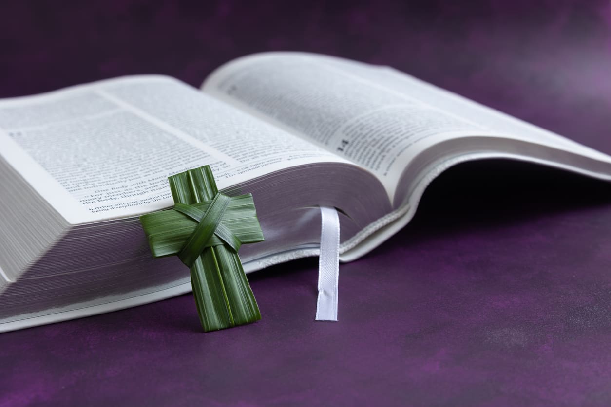 An open Bible with a woven palm cross, symbolizing Palm Sunday's connection to faith, scripture, and the start of Holy Week.