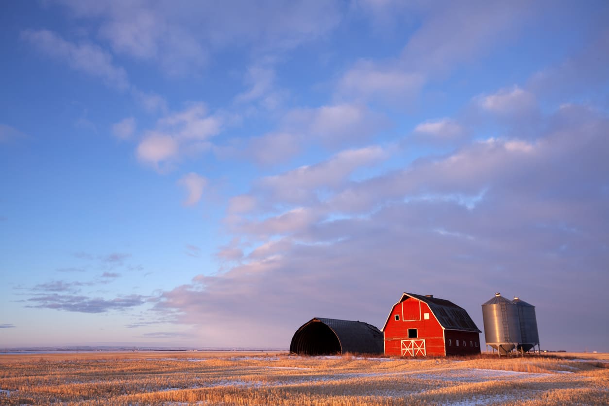 A picturesque Saskatchewan prairie farm with a red barn, open fields, and a vast sky, capturing the province's agricultural heritage.