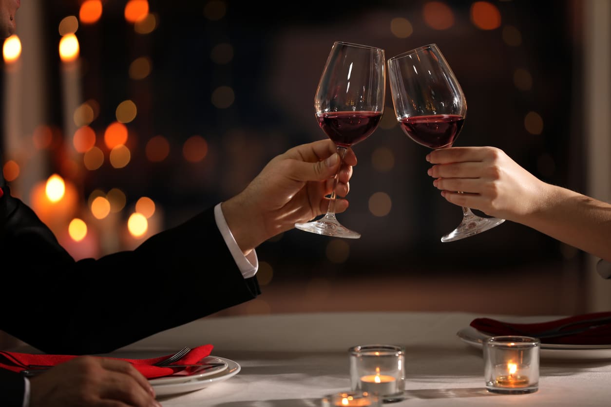 A couple clinks wine glasses in a romantic, candlelit setting, capturing the intimate essence of Valentine's Day.