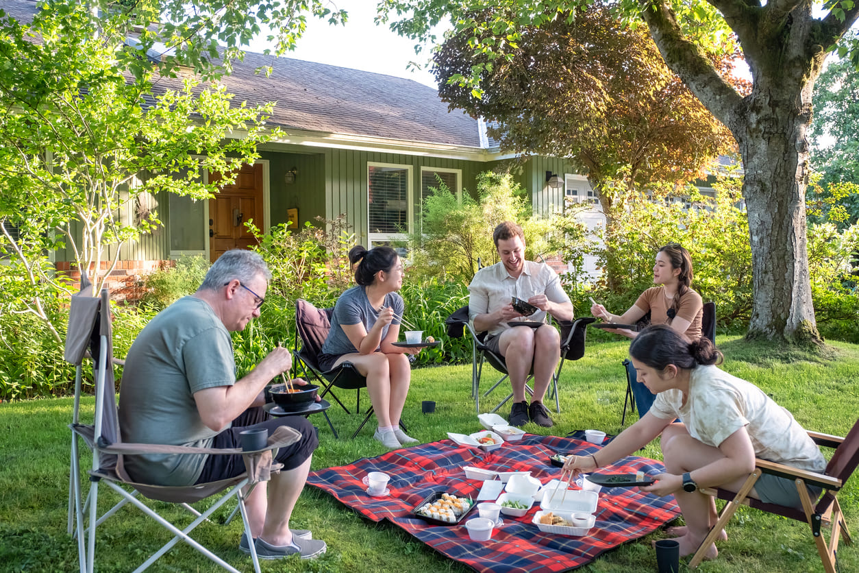 A cheerful family gathers in a lush backyard, enjoying a relaxed outdoor picnic on a warm Victoria Day afternoon.