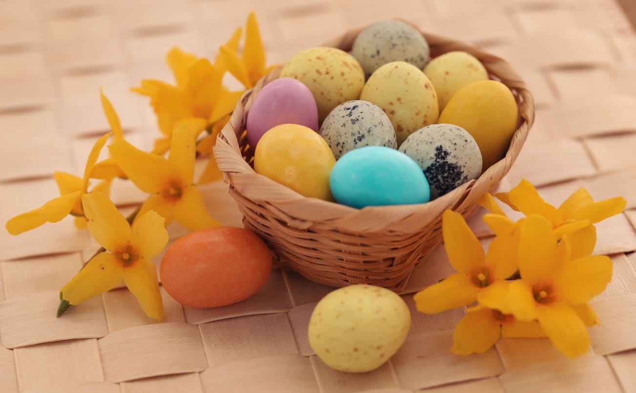 A wicker basket of colorful Easter eggs surrounded by bright yellow flowers, symbolizing spring and celebration.