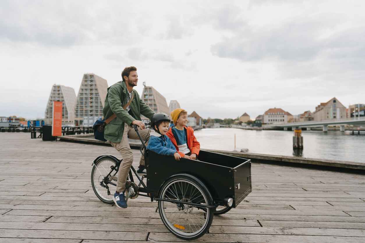 A father rides a cargo bike with his two children, enjoying a joyful moment together in an urban Danish setting.