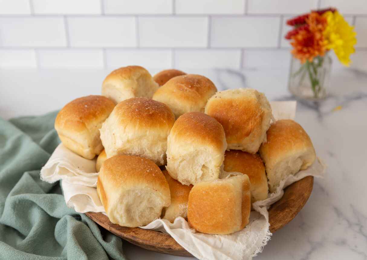 A wooden plate filled with golden-brown, fluffy wheat buns.