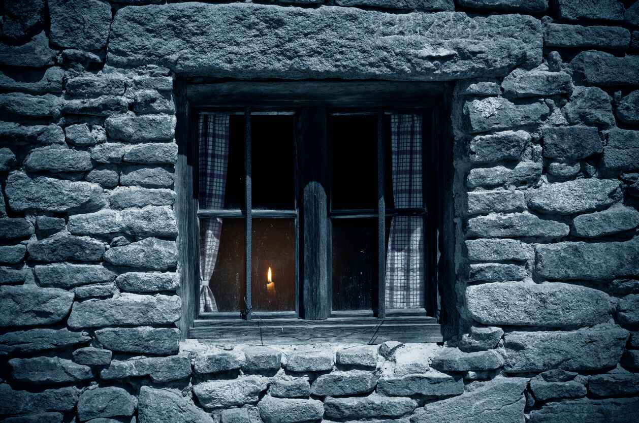 A dimly lit stone house with a single candle glowing in the window, symbolizing Denmark's Liberation Day and the return of freedom.