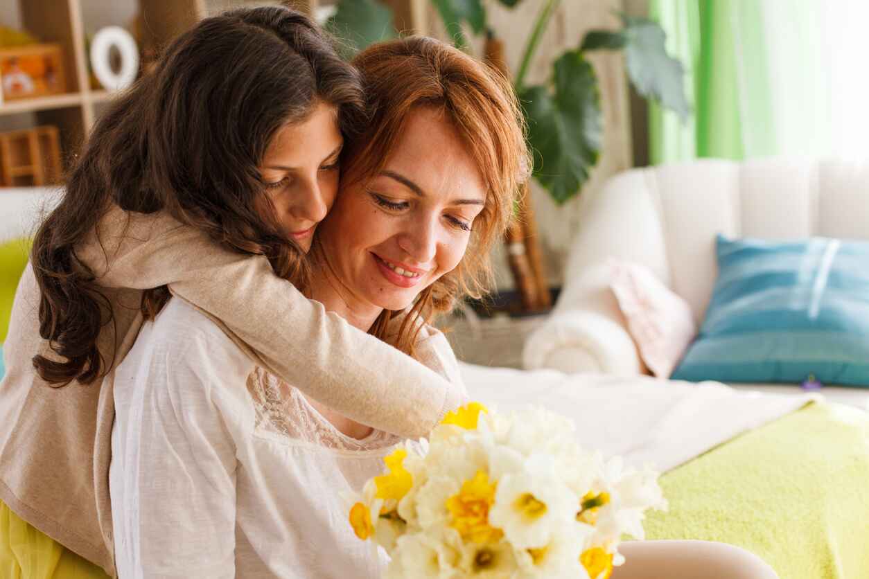 A warm Mother's Day scene where a daughter lovingly embraces her mother, gifting her a bouquet of fresh flowers in a cozy home setting.