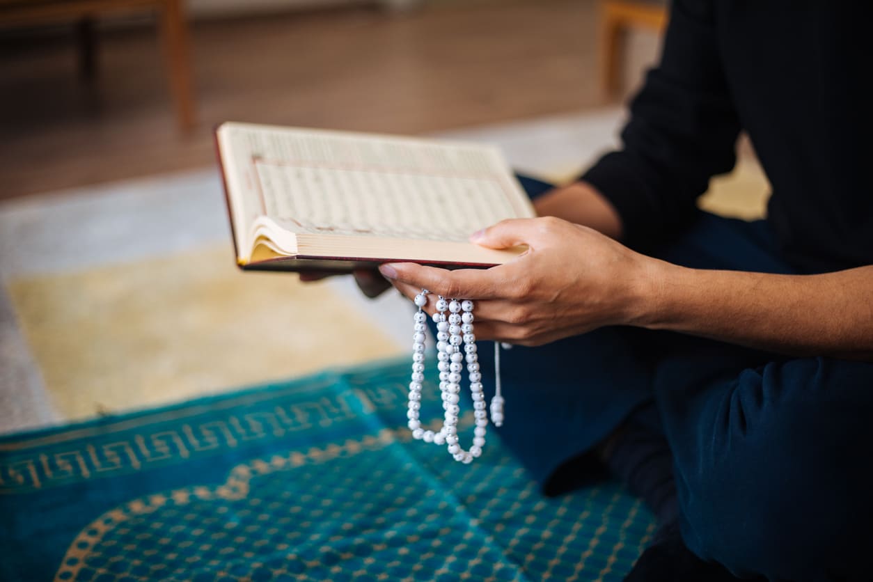 A person seated on a prayer mat, holding prayer beads and the Quran, immersed in peaceful worship and reflection.