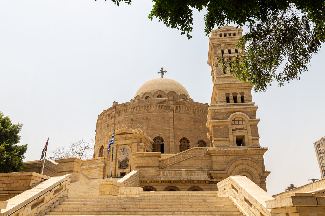 A striking view of the historic Church of St. George in Cairo, framed by palm trees and ancient stone walls.