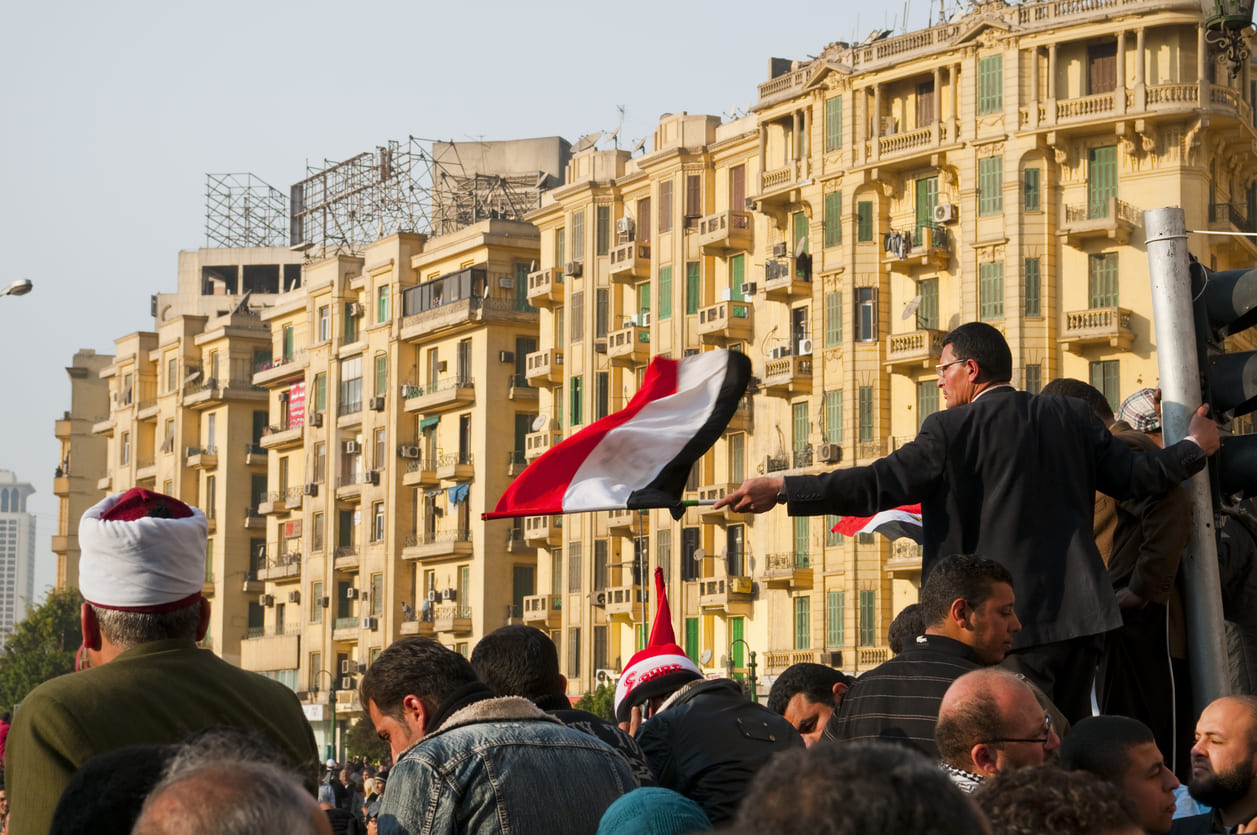 A crowd gathered in an urban square, with Egyptian flags raised high, symbolizing unity, pride, and the spirit of Labor Day.