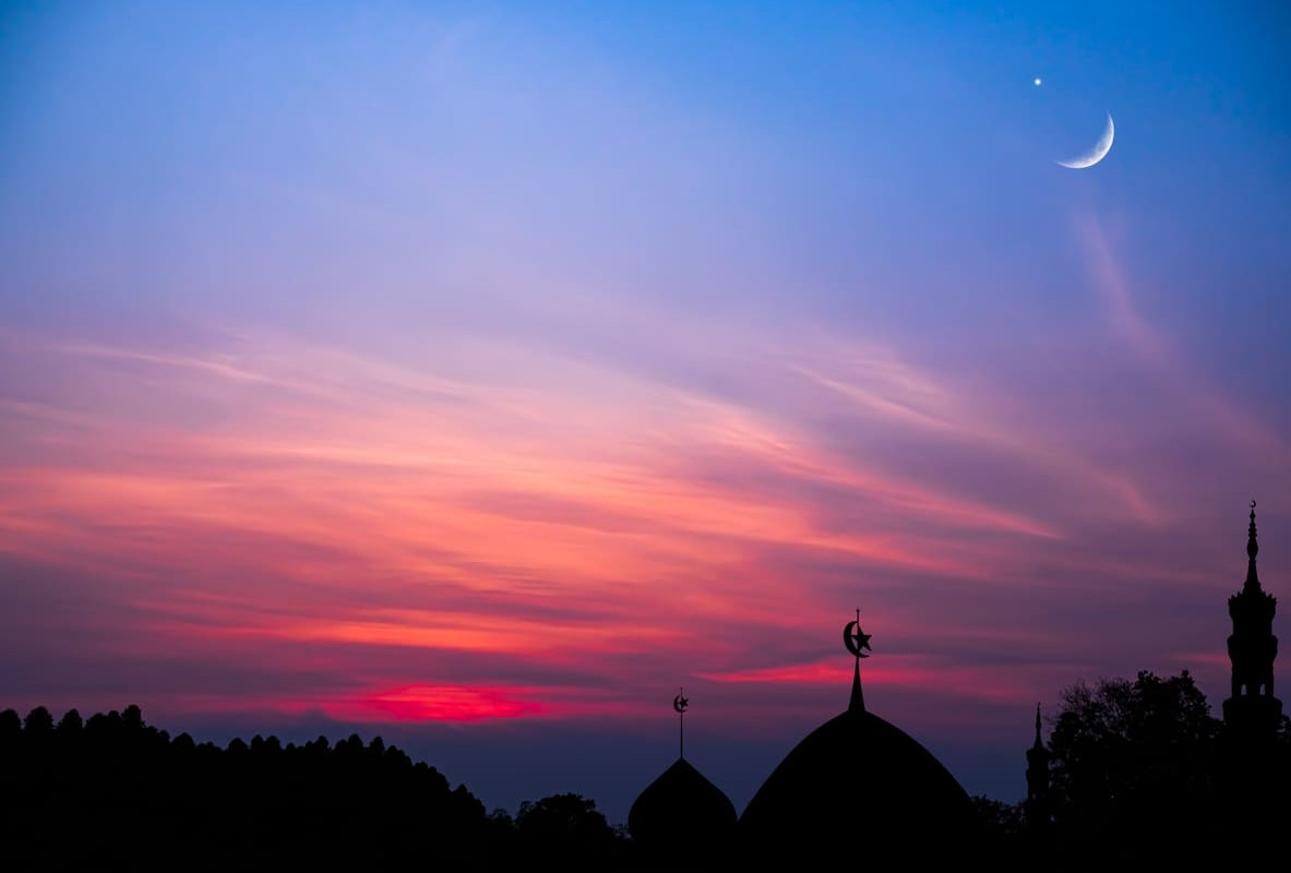 A serene twilight sky with a crescent moon shining above silhouetted mosque domes, capturing the spiritual essence of Muharram.