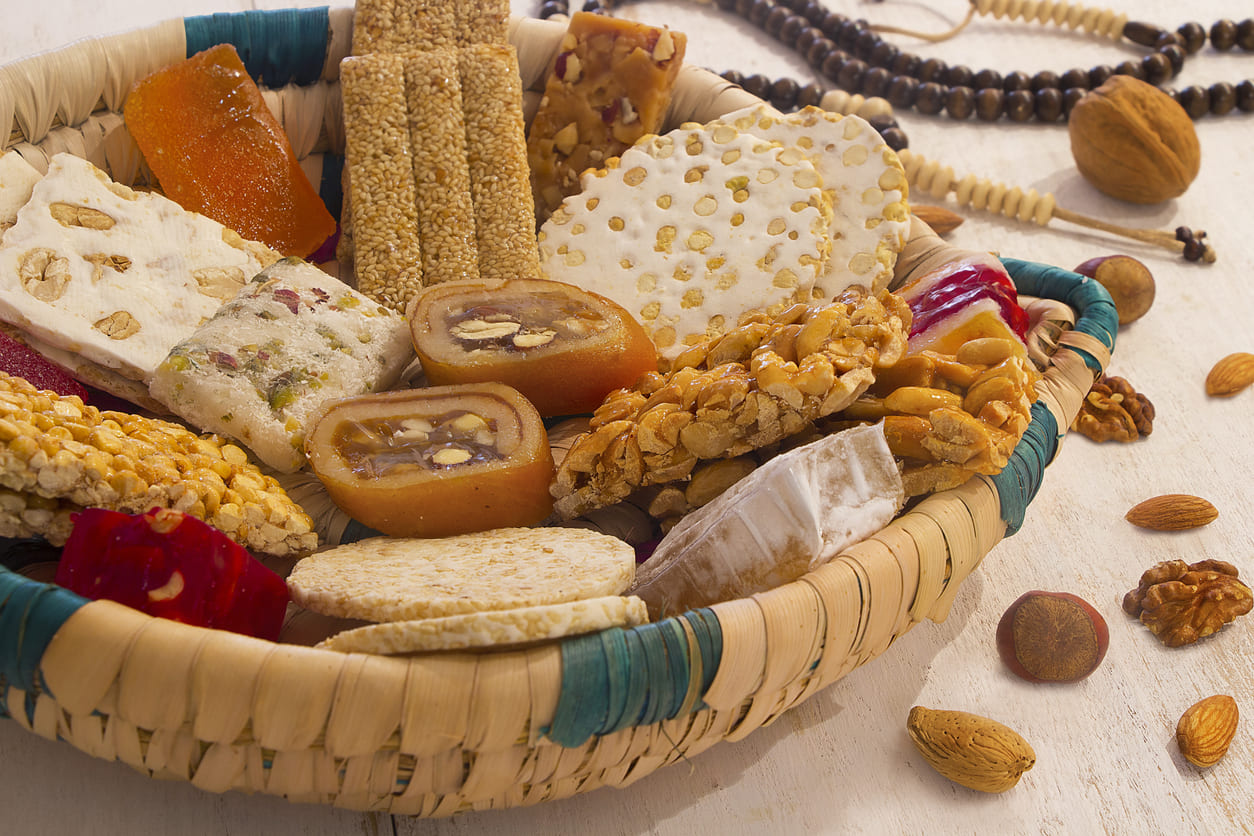 A colorful assortment of traditional Egyptian sweets, displayed in a woven basket alongside prayer beads and nuts.