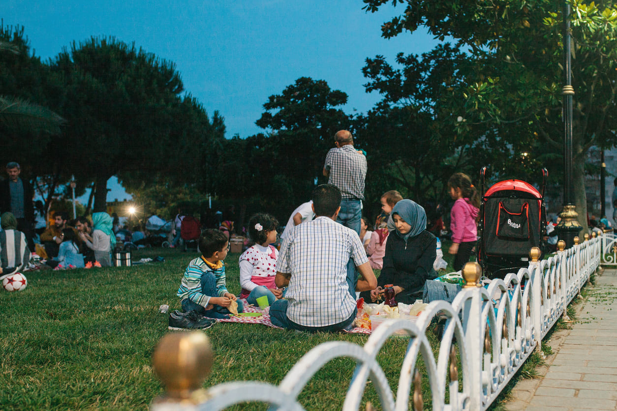 A lively park scene showing families gathered on the grass, sharing food and enjoying the evening breeze during Sham El-Nessim.