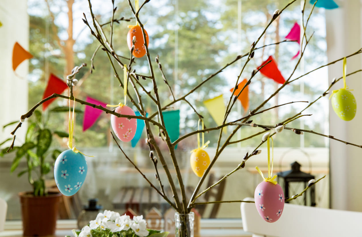 A budding Easter tree decorated with colorful hanging eggs stands in a sunlit Finnish home, symbolizing the arrival of spring and Easter joy.