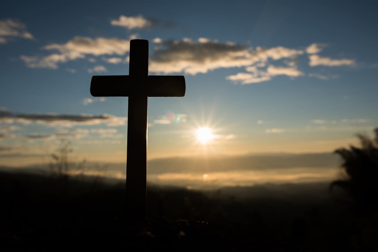 A simple wooden cross stands against a sunrise sky, symbolizing the solemnity and spiritual reflection of Good Friday.