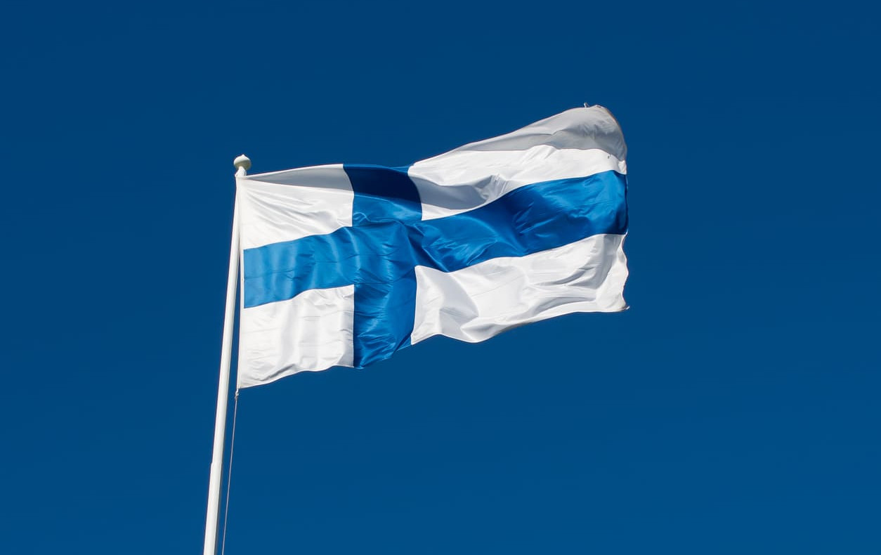 A Finnish flag flutters on a tall pole against a clear winter sky, reflecting the solemn pride of Finland's Independence Day.