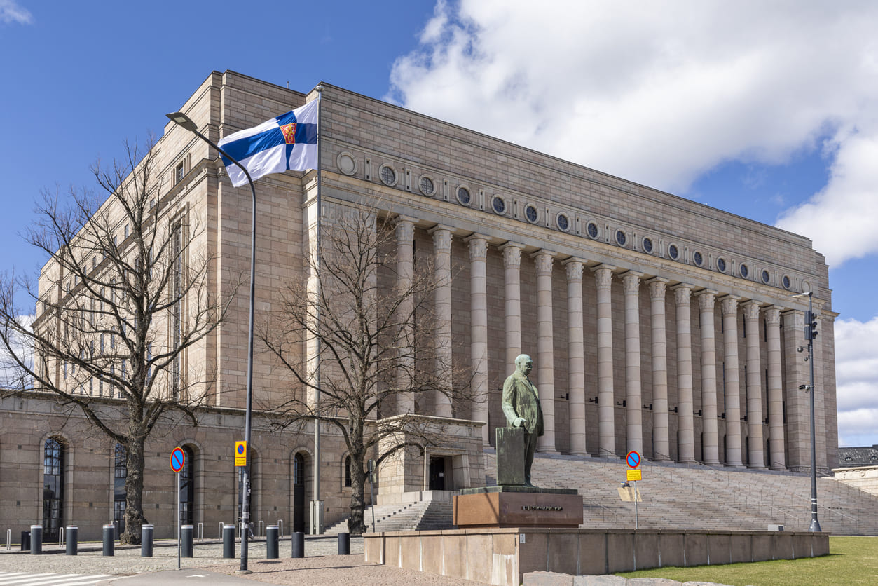 The Finnish Parliament House with the state flag fluttering in the spring breeze, reflecting the nation's heartfelt tribute to mothers.