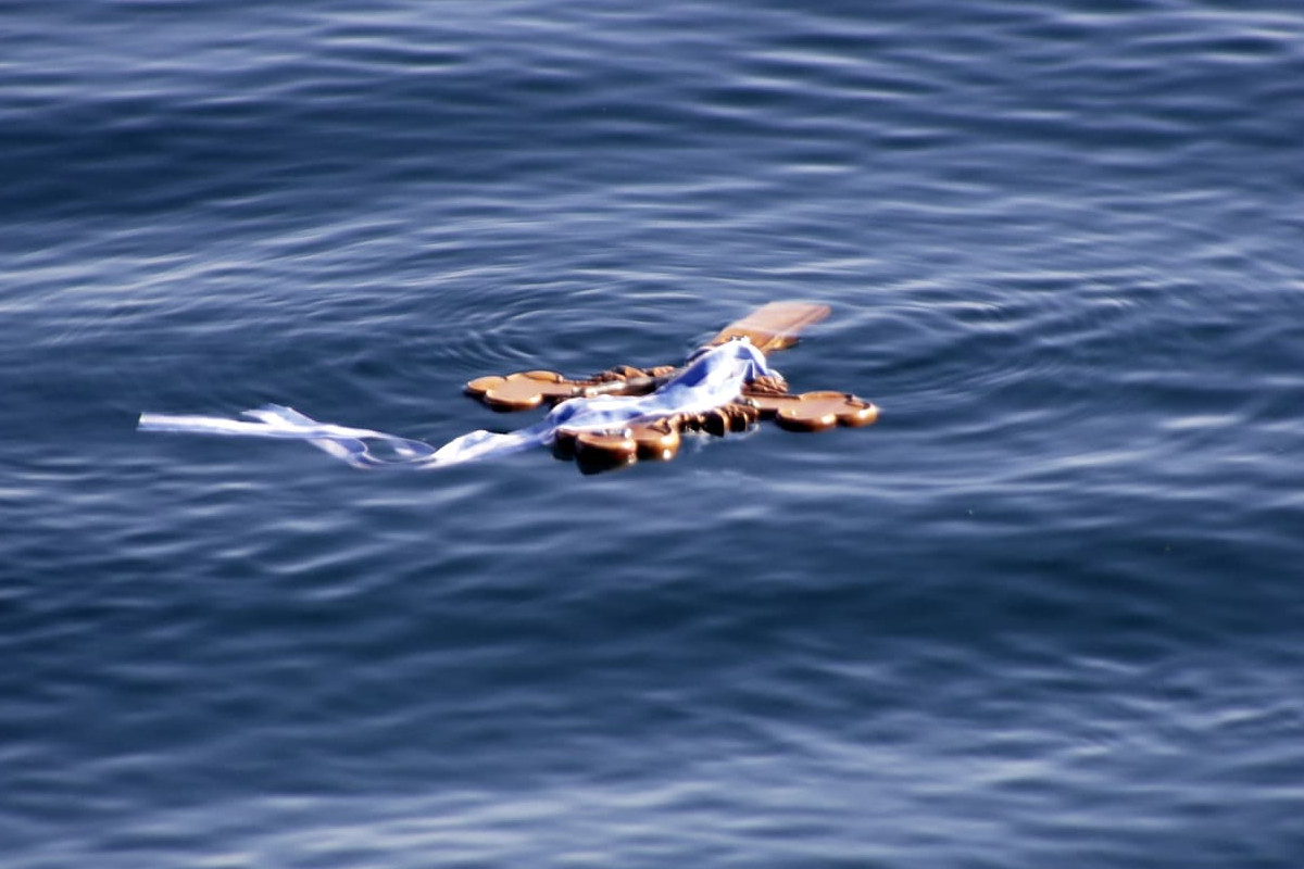 A close-up of a wooden cross with ribbons floating on calm blue water, symbolizing the Epiphany ritual of the Blessing of the Waters.