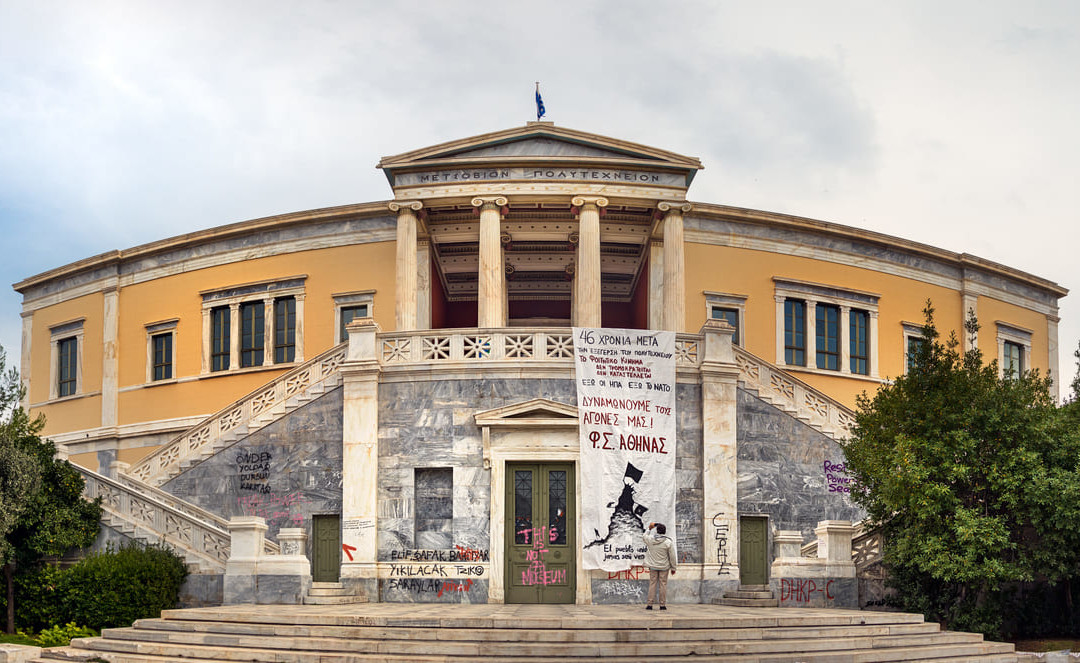 The iconic facade of the Athens Polytechnic is seen draped with banners and graffiti, echoing the spirit of the 1973 student uprising.