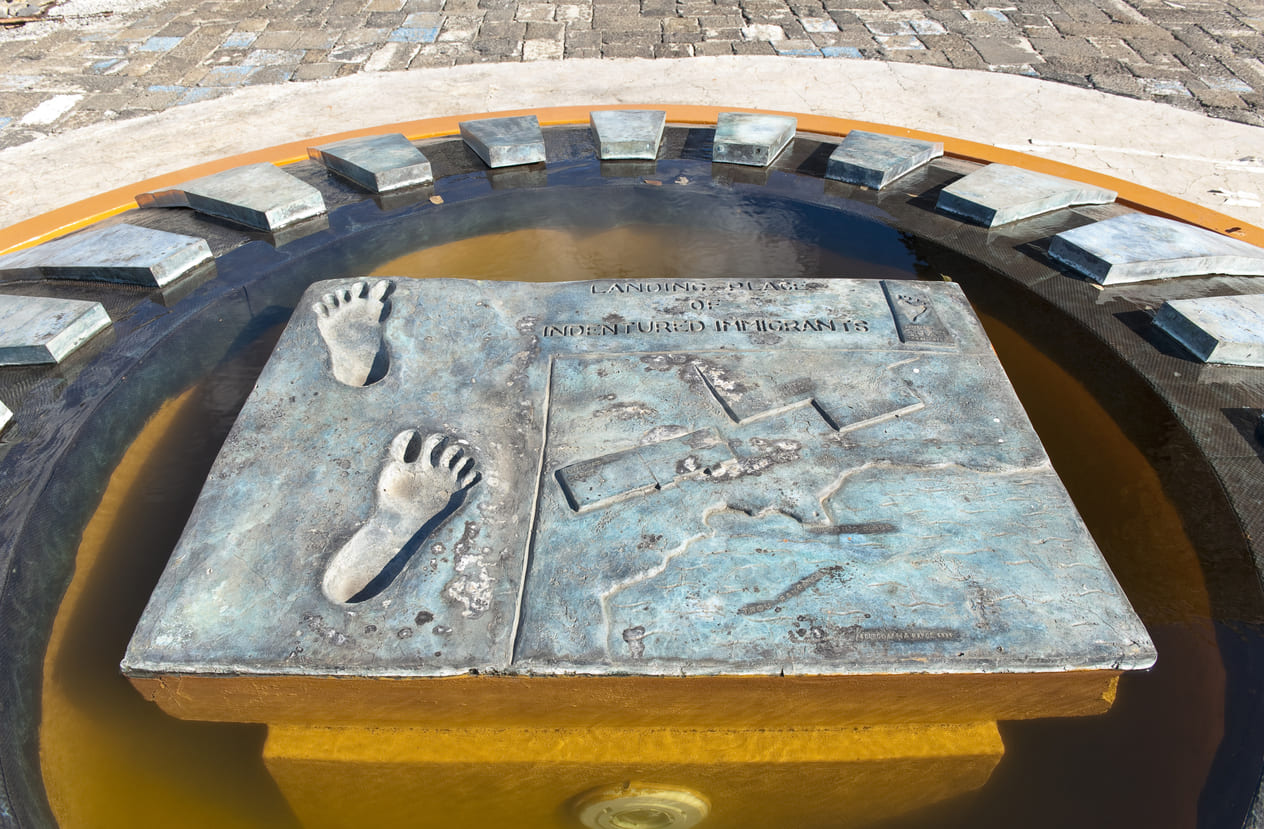 A bronze plaque with engraved footprints and a map, set in water at Aapravasi Ghat, symbolizing the landing site of Indian indentured laborers in Mauritius.