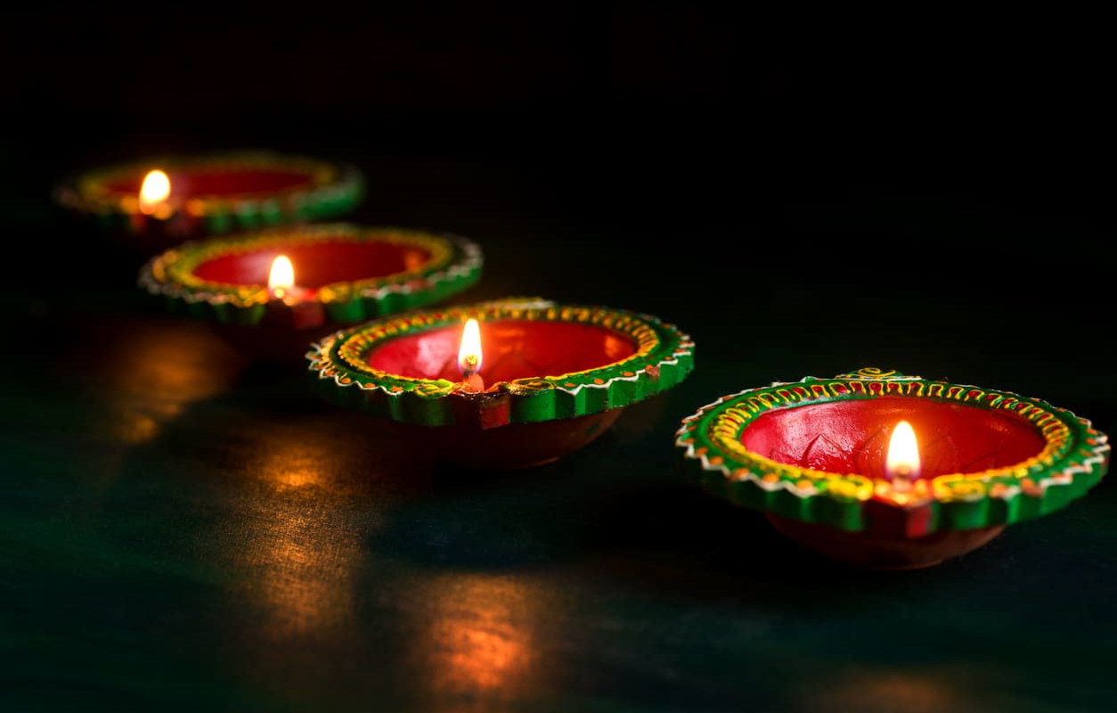 A row of beautifully decorated oil lamps glowing warmly in the dark, symbolizing the festive and spiritual essence of Divali.