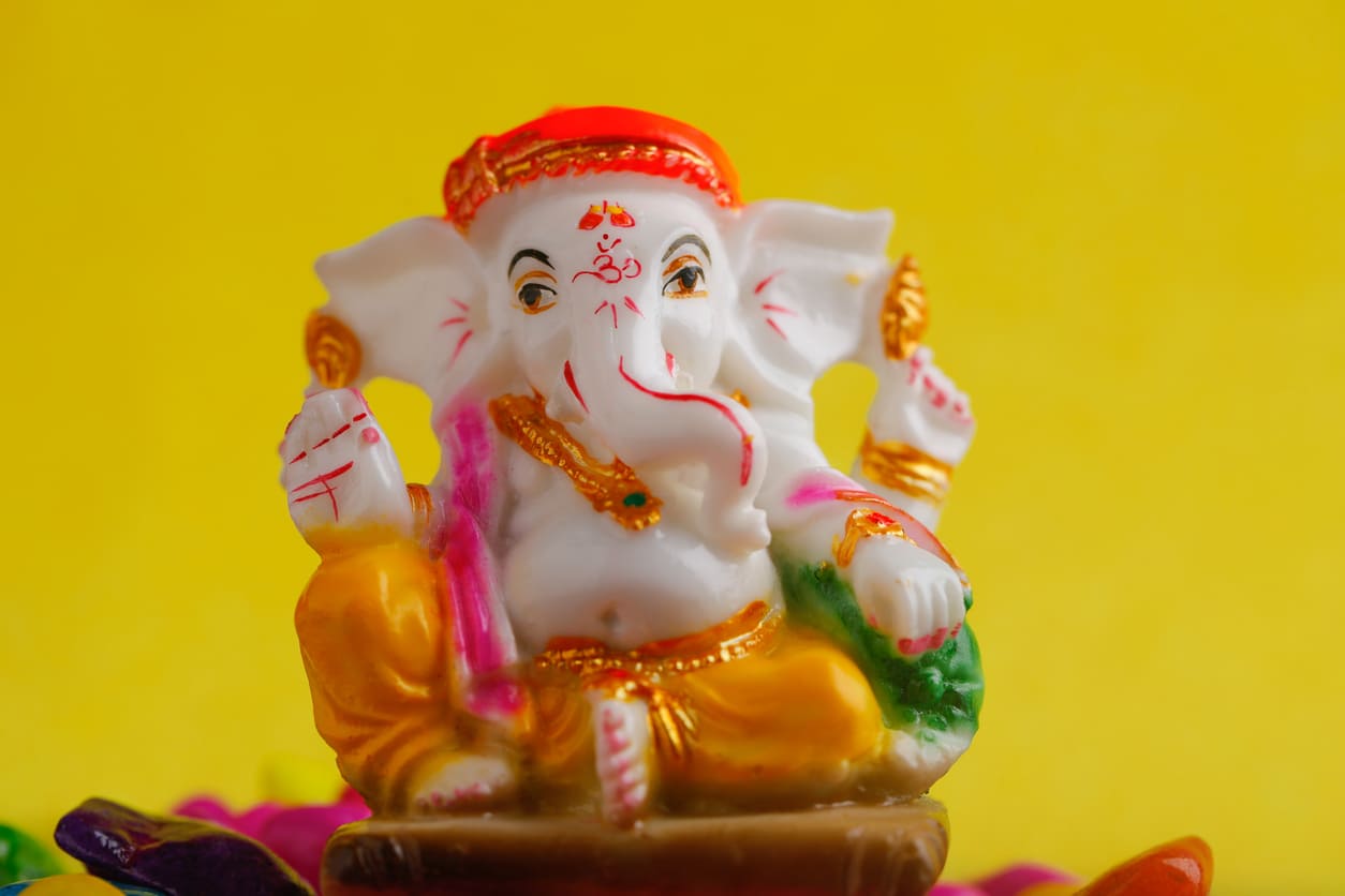 A colorful clay idol of Lord Ganesha with intricate details, set against a bright yellow background, symbolizing festivity and devotion.