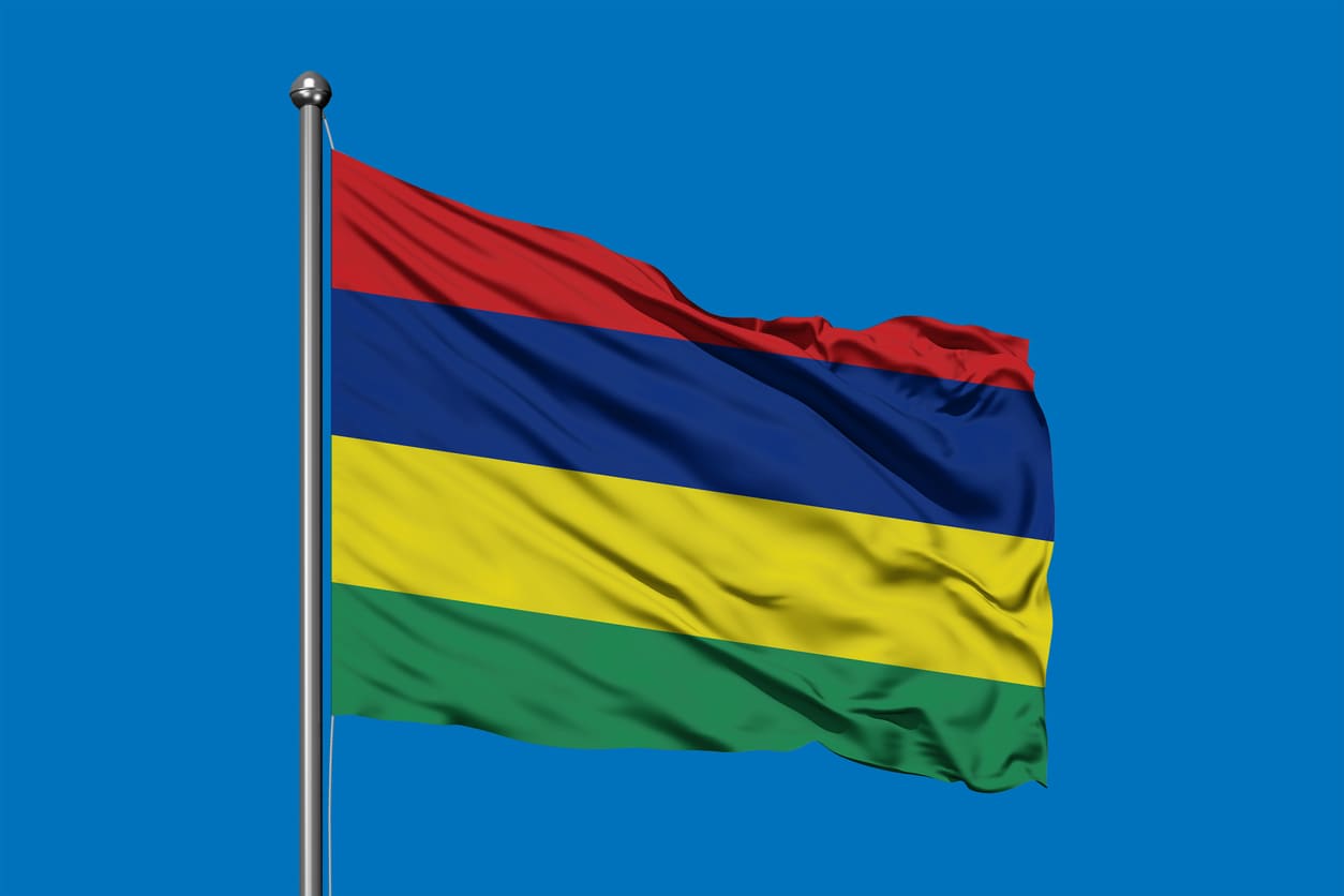 The vibrant national flag of Mauritius, with its red, blue, yellow, and green stripes, waves against a clear blue sky, embodying the spirit of Independence and Republic Day.