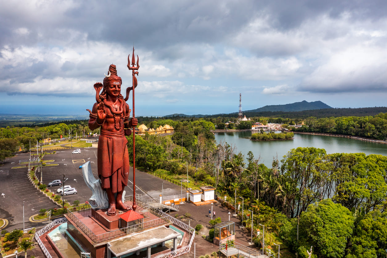 A towering statue of Lord Shiva overlooks the serene Grand Bassin (Ganga Talao), surrounded by lush greenery and temple structures.