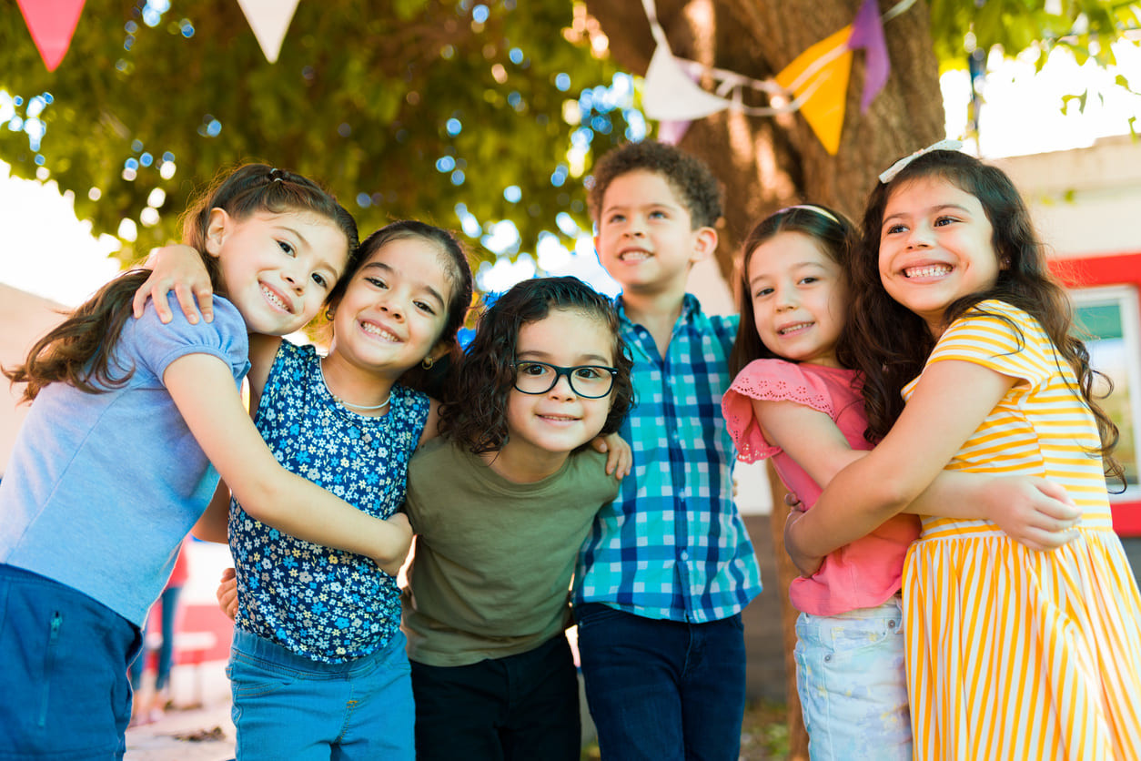 A group of cheerful children hugging and smiling under festive decorations, capturing the joyful spirit of Children's Day in Mexico.