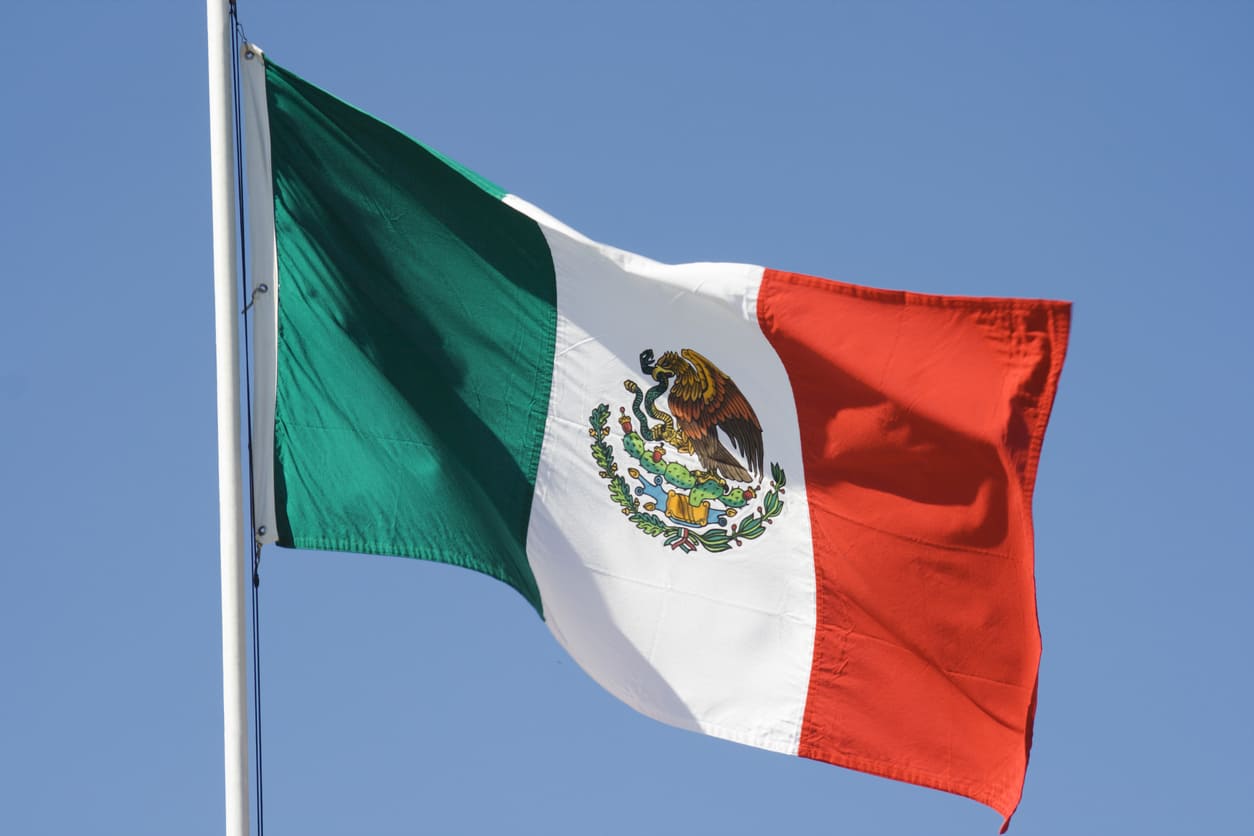 Mexican flag fluttering in the wind against a clear blue sky, representing national pride and identity.