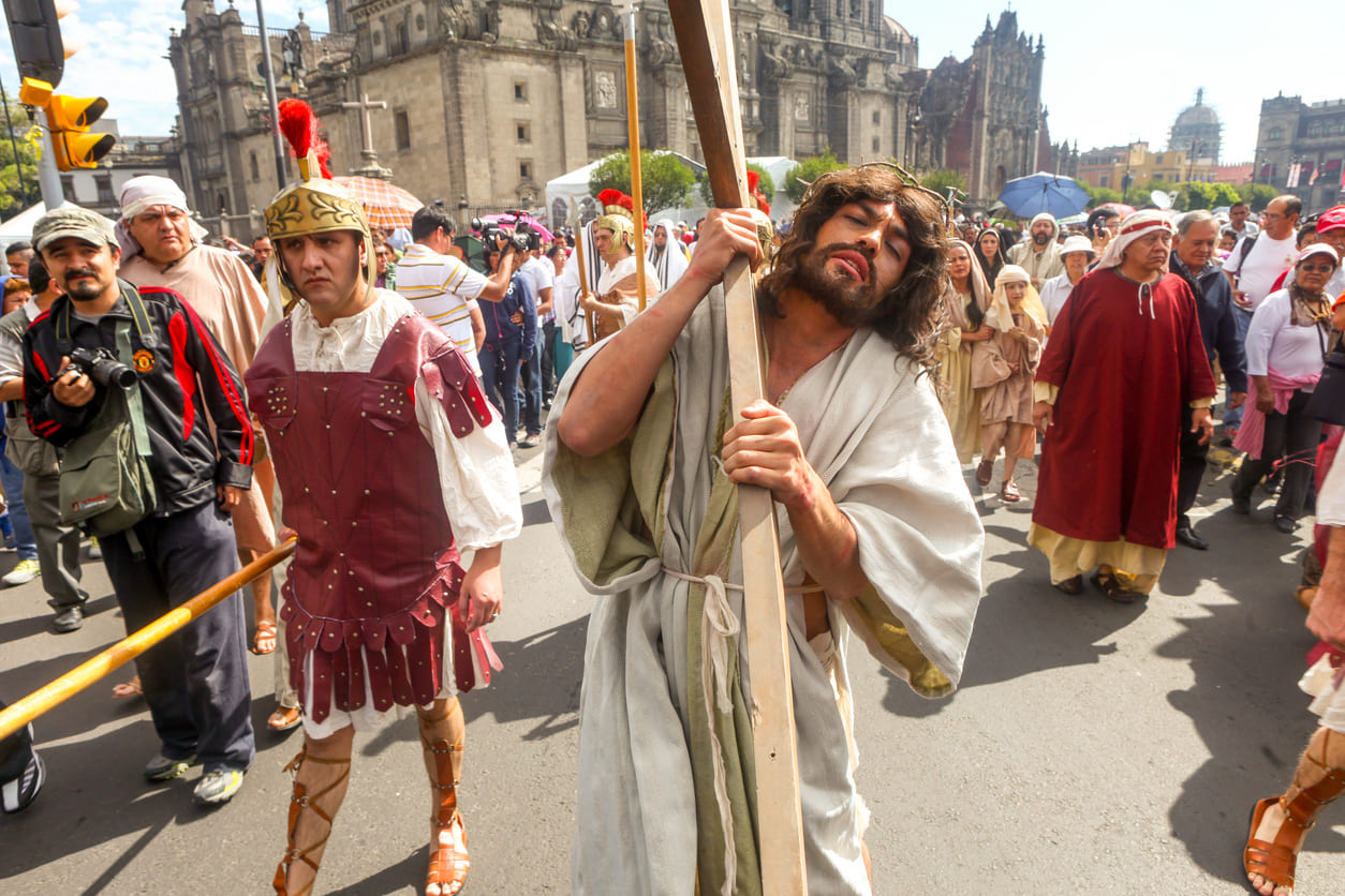 A dramatic reenactment of Jesus carrying the cross through crowded streets, surrounded by actors and onlookers during Good Friday in Mexico.
