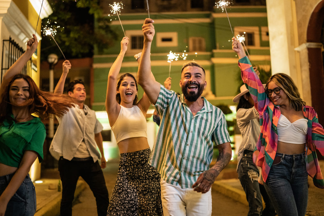 A group of smiling friends holding sparklers as they celebrate New Year's Eve on a lively street in Mexico.