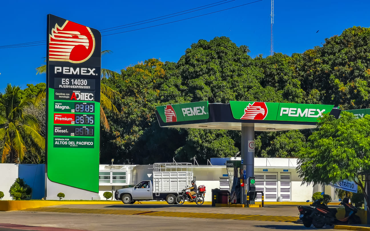 A PEMEX gas station surrounded by greenery and a clear blue sky symbolizes Mexico's national oil company, created after the 1938 oil expropriation.