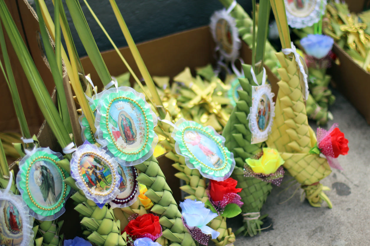 Beautifully woven palm fronds adorned with saint images and colorful flowers, prepared for Palm Sunday blessings in Mexico.