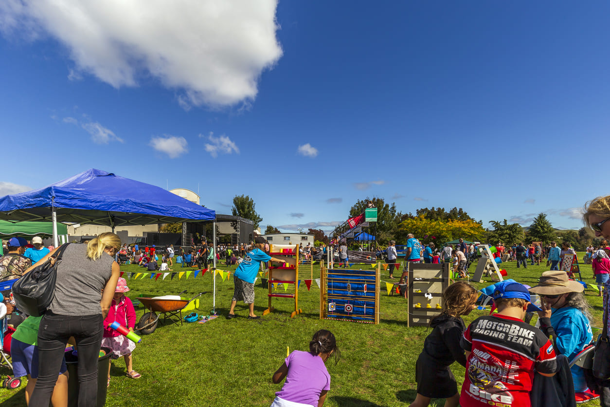 A bustling outdoor community event with families and children engaging in games and activities on Easter Monday in New Zealand.