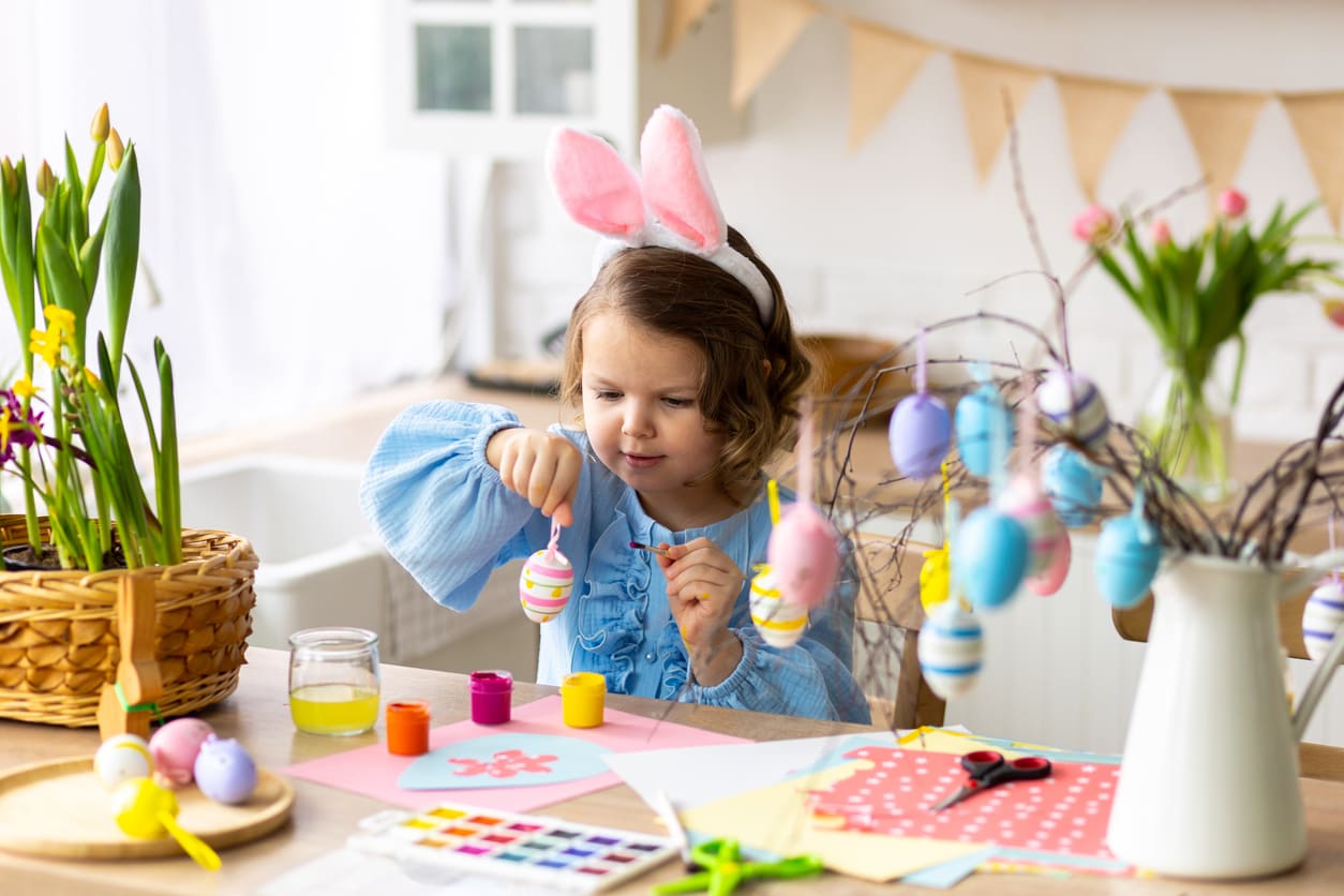 A cheerful child decorates Easter eggs at a festive table, showcasing the playful and creative spirit of Easter Sunday in New Zealand.