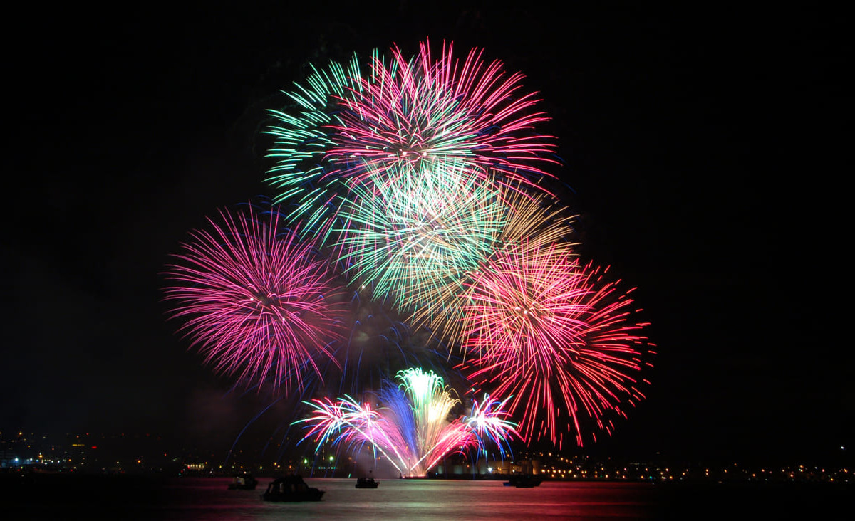 Vibrant fireworks burst over the Hauraki Gulf, reflecting on the water and illuminating the night during Guy Fawkes Night festivities.
