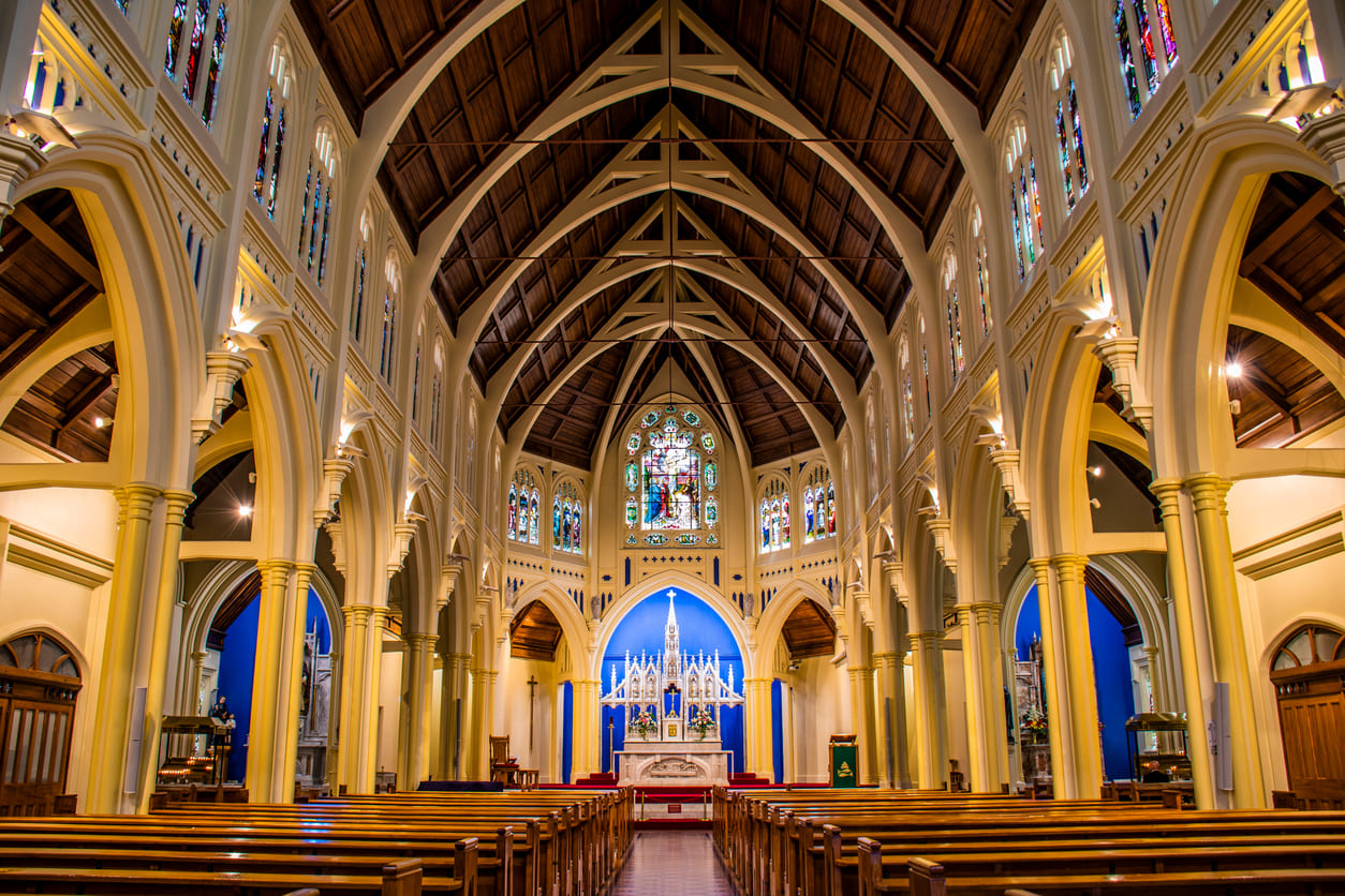 The grand interior of a Catholic Church in central Wellington, adorned with stained glass and soft lighting, reflecting the solemn atmosphere of Holy Saturday.
