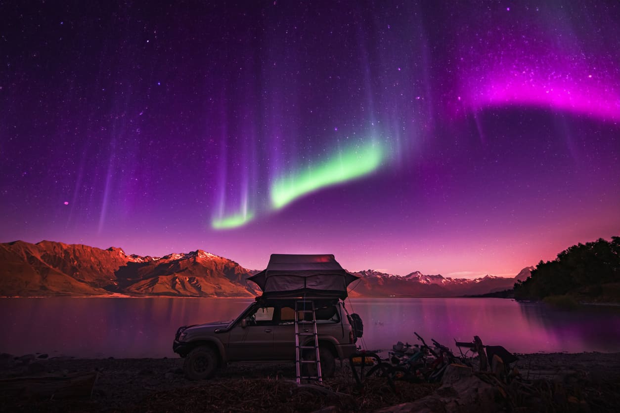 A lone camper gazes at a dazzling starry sky and auroras, capturing the spirit of reconnecting with nature during Matariki in New Zealand.