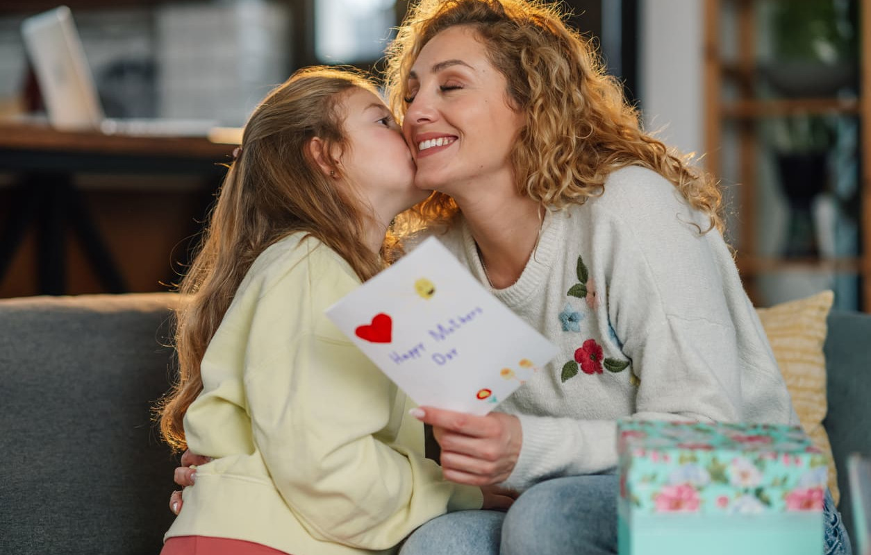 A mother and daughter share a tender moment with a handmade Mother's Day card and a beautifully wrapped gift.