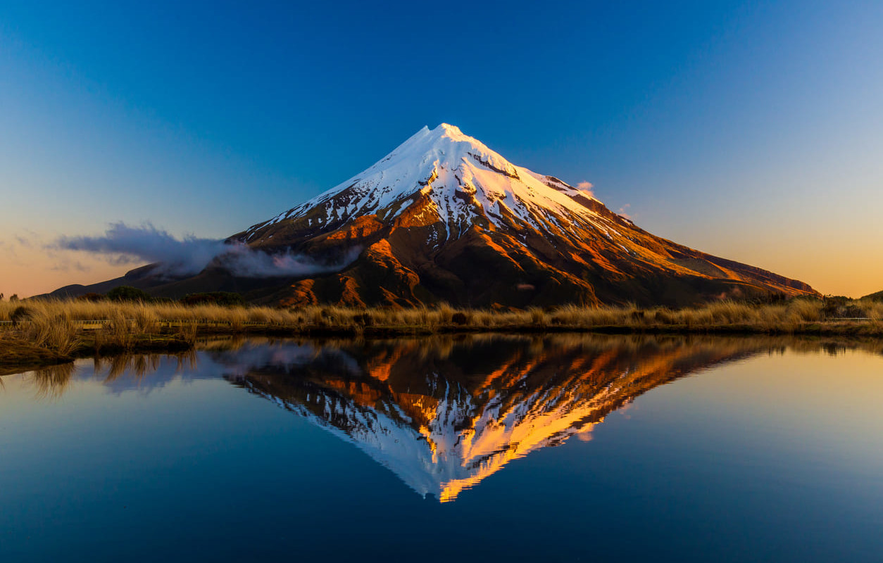 A breathtaking view of snow-capped Mount Taranaki mirrored in calm waters, showcasing the natural beauty of the Taranaki region.