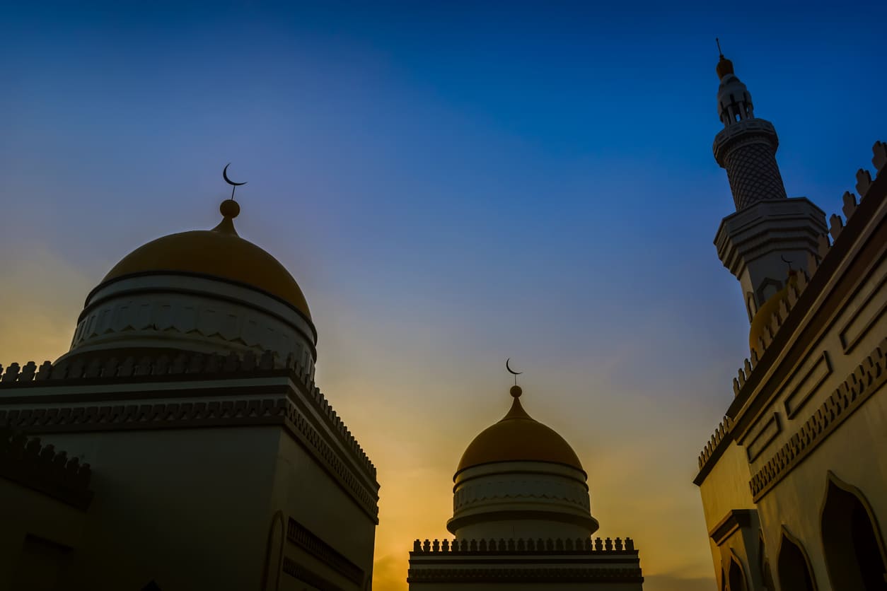A mosque with golden domes and a minaret beautifully outlined against a colorful evening sky.