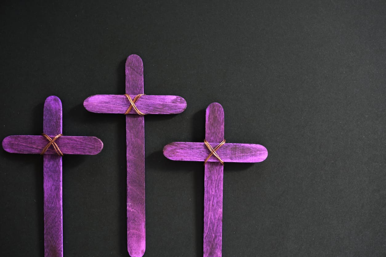 Three handcrafted purple crosses rest against a dark background, symbolizing the quiet mourning and hope of Black Saturday.