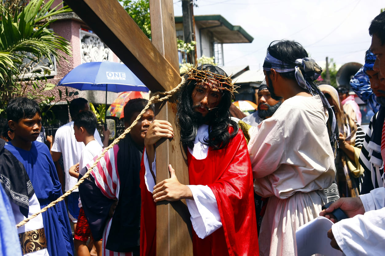 A man portraying Jesus carries a wooden cross during a traditional Good Friday reenactment surrounded by devotees in the Philippines.