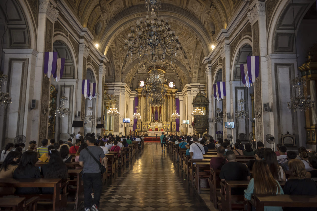 Faithful attend a solemn Maundy Thursday service inside the historic San Agustin Church, surrounded by purple drapes symbolizing penance and reflection.