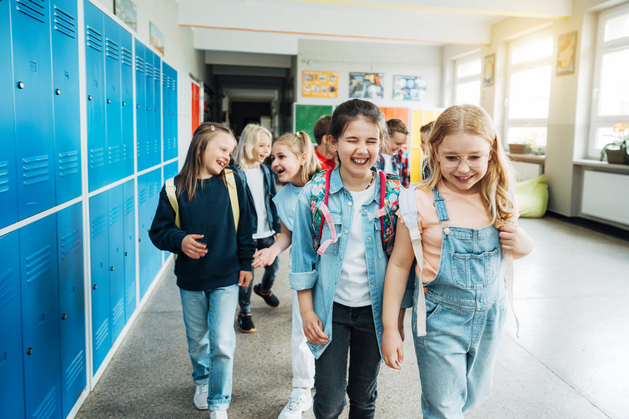 A group of cheerful children walk through a brightly lit school hallway, laughing and enjoying a joyful moment together.