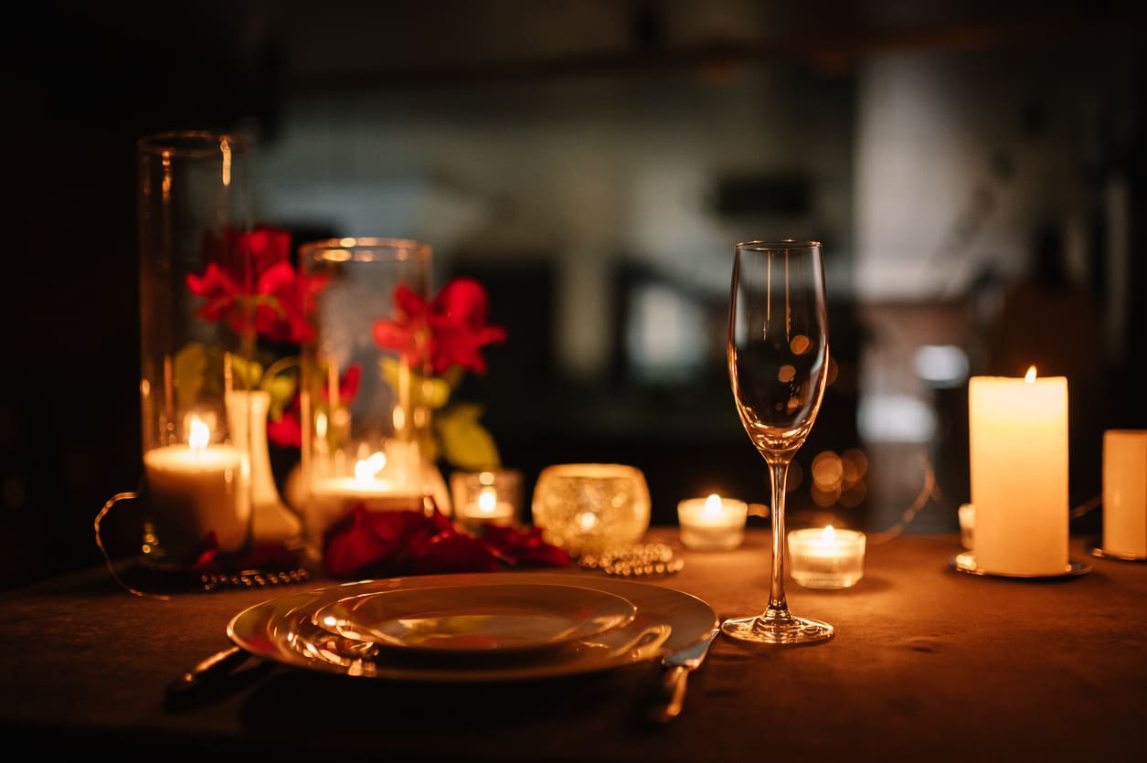 A warmly lit, romantic dinner setup with candles, roses, and elegant tableware.