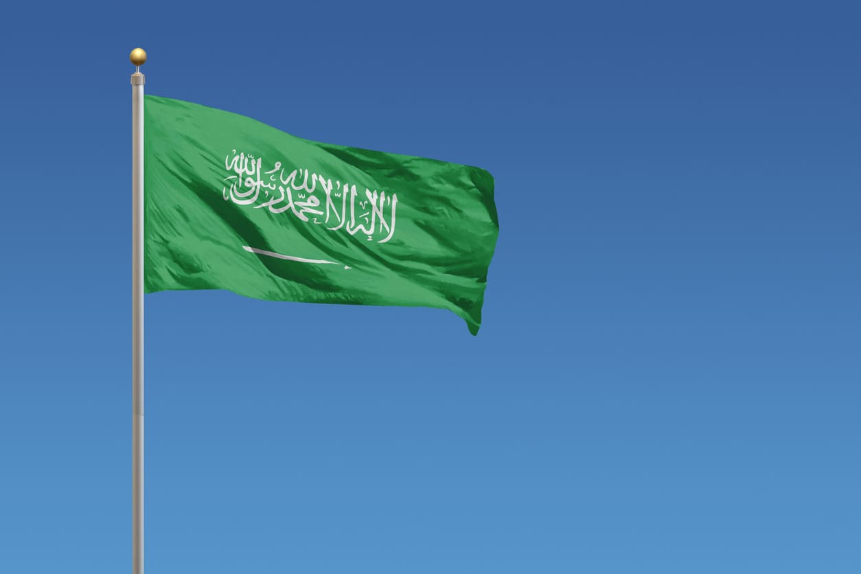 The Saudi Arabian flag flying against a clear blue sky, symbolizing national pride and heritage.
