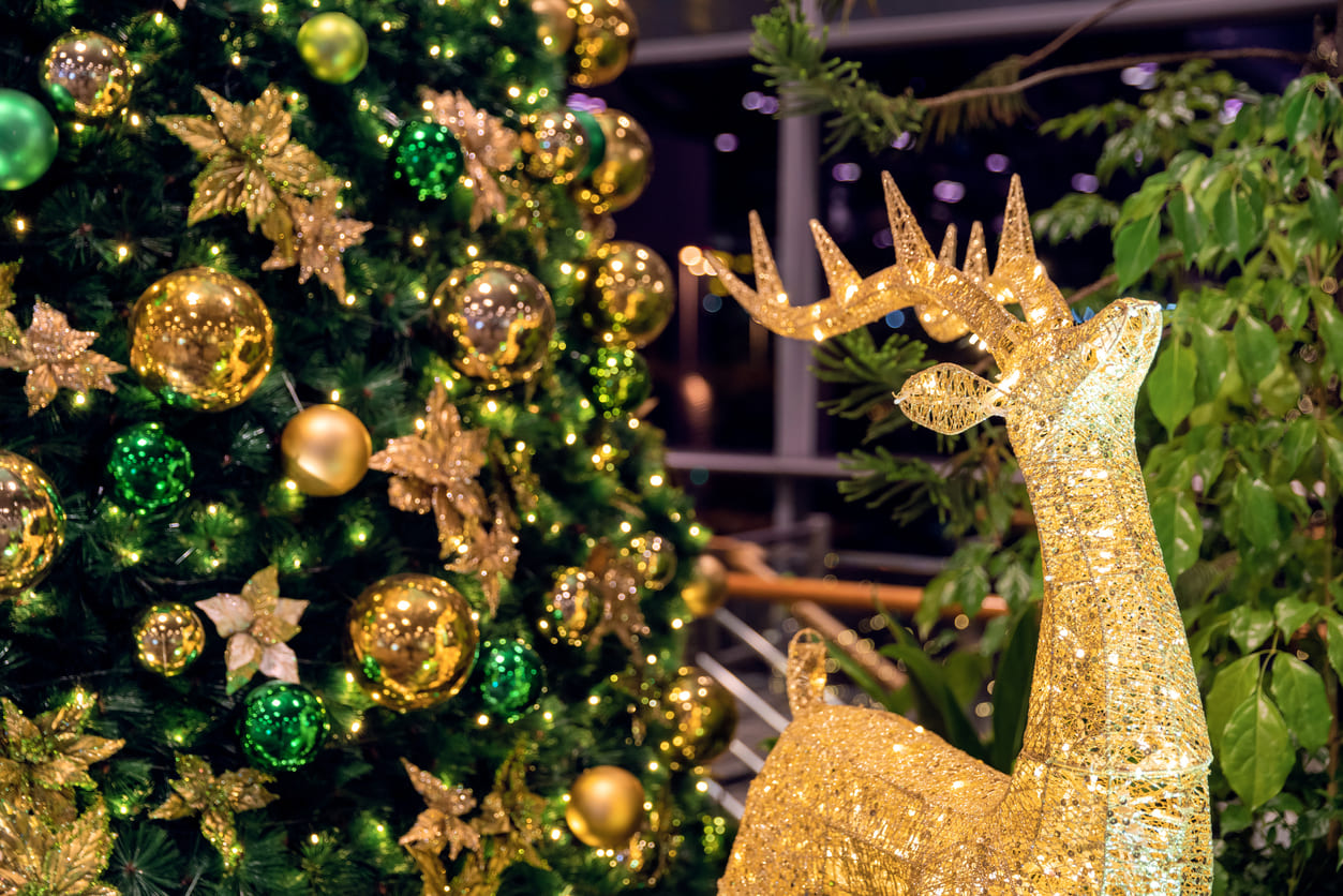 A sparkling Christmas tree decorated with golden and green ornaments next to a glowing reindeer figure, creating a festive holiday atmosphere.
